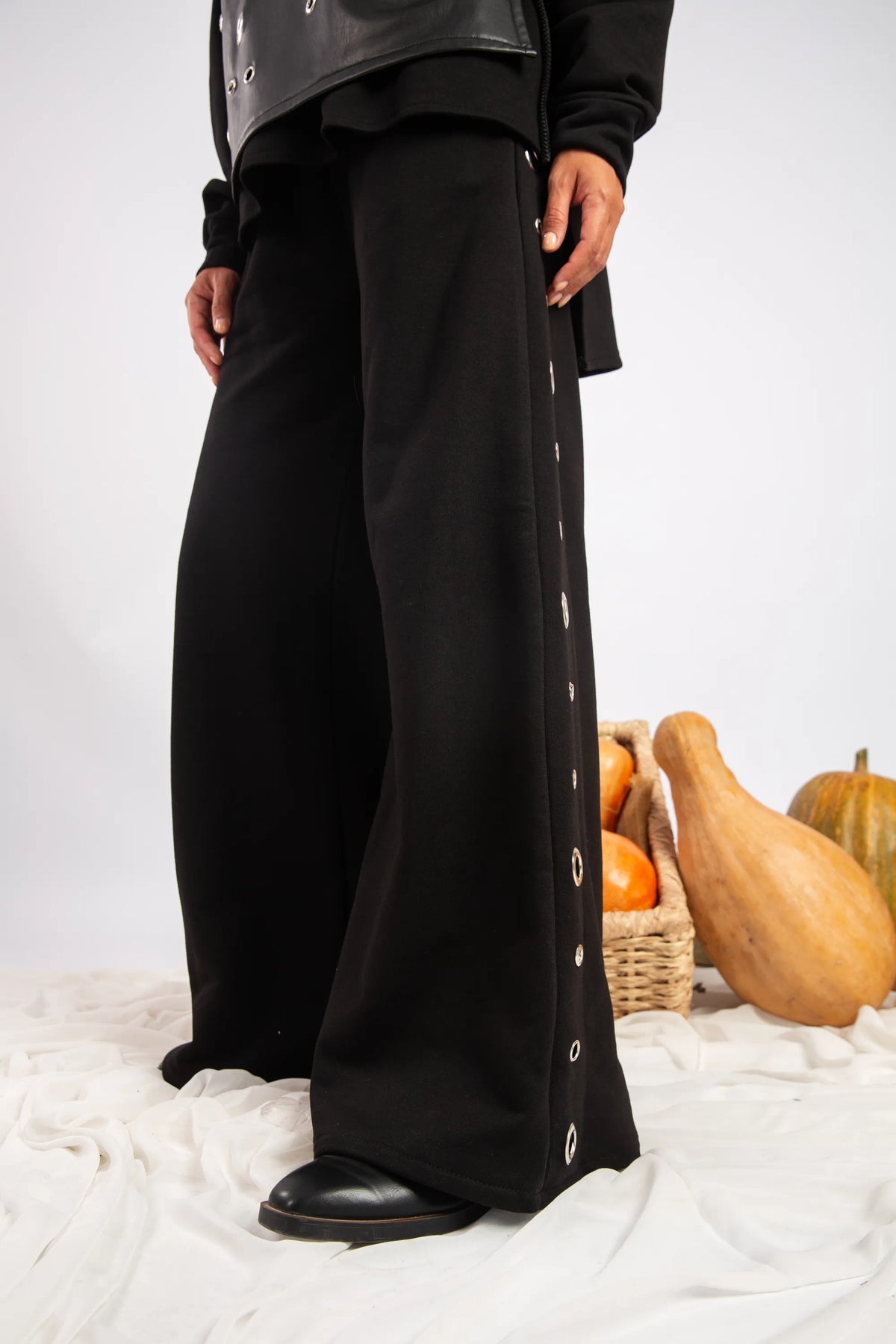 Person wearing black wide-leg pants with button details on a white background with pumpkins.