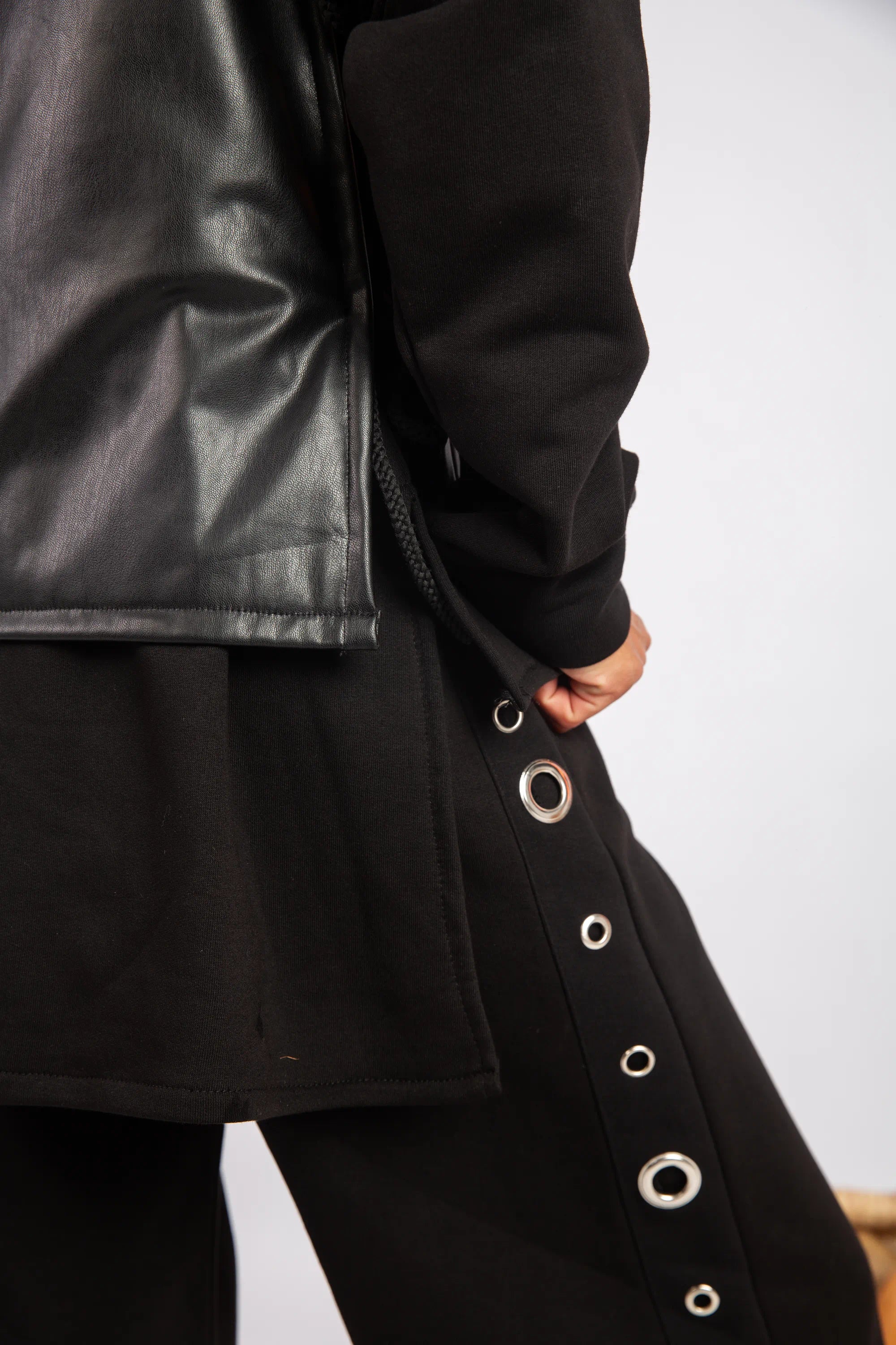 Close-up of a black coat with grommet details on a plain background