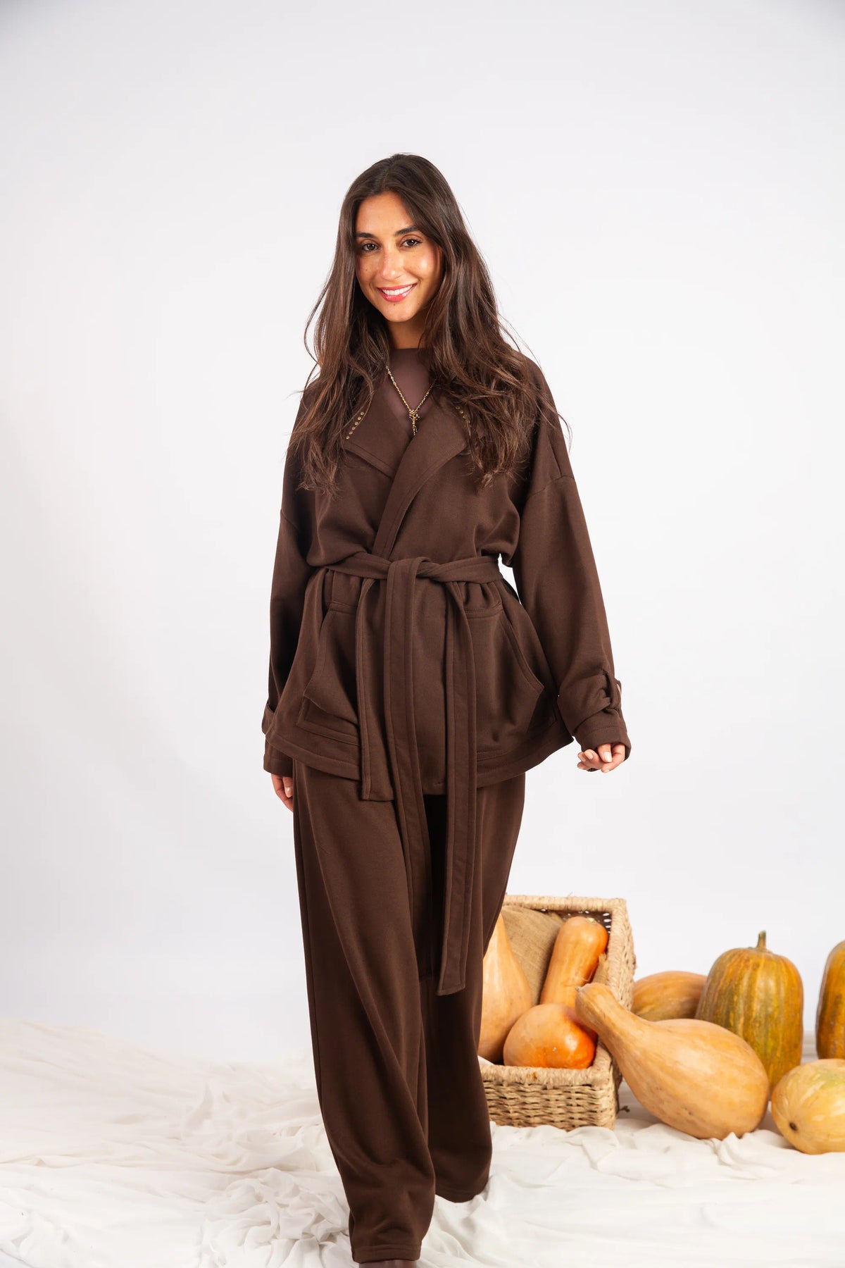 Woman wearing a brown outfit standing next to a basket of gourds on a white background