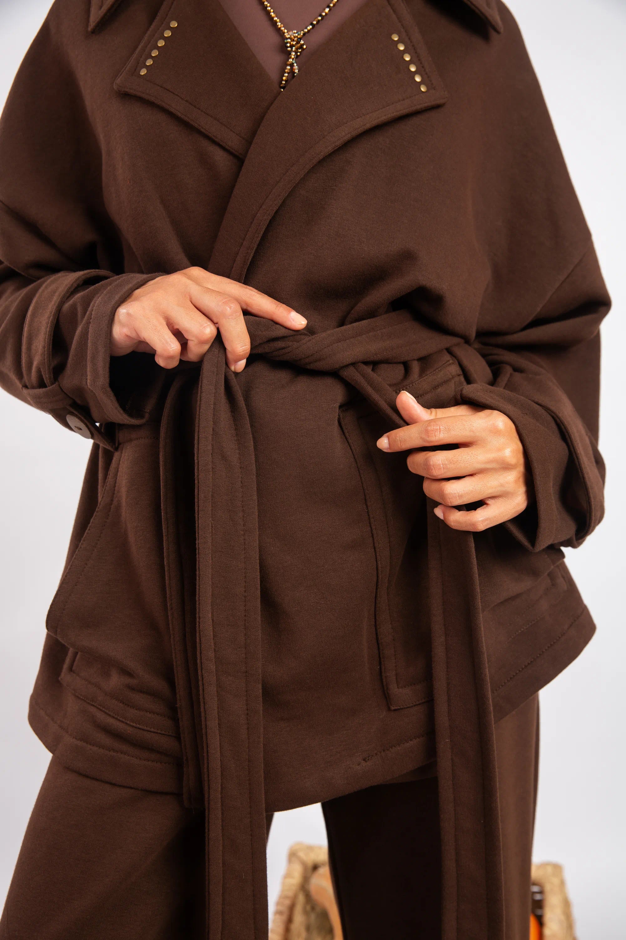 Brown coat with a belt being adjusted on a white background
