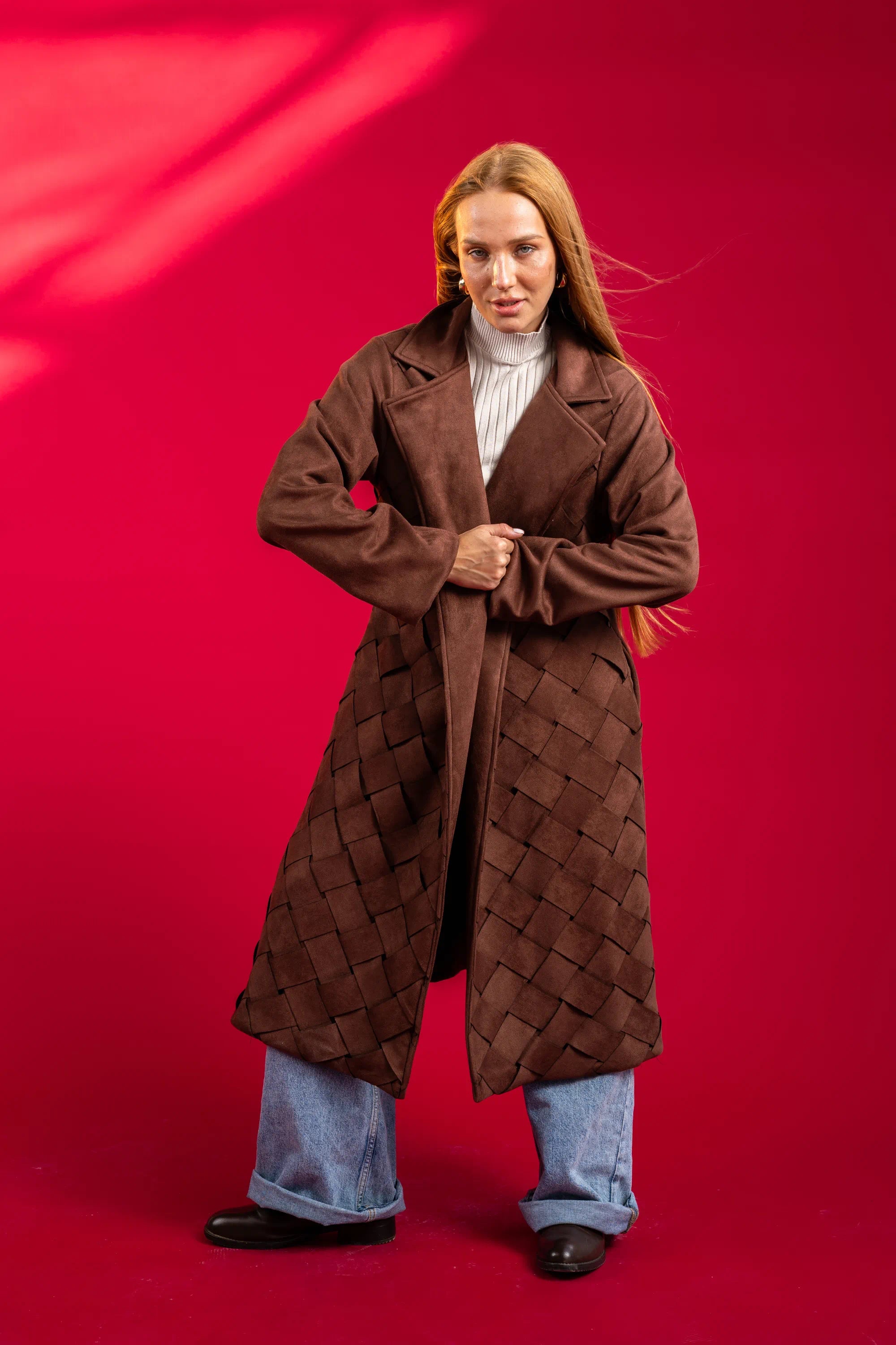 Person wearing a long brown coat against a red background