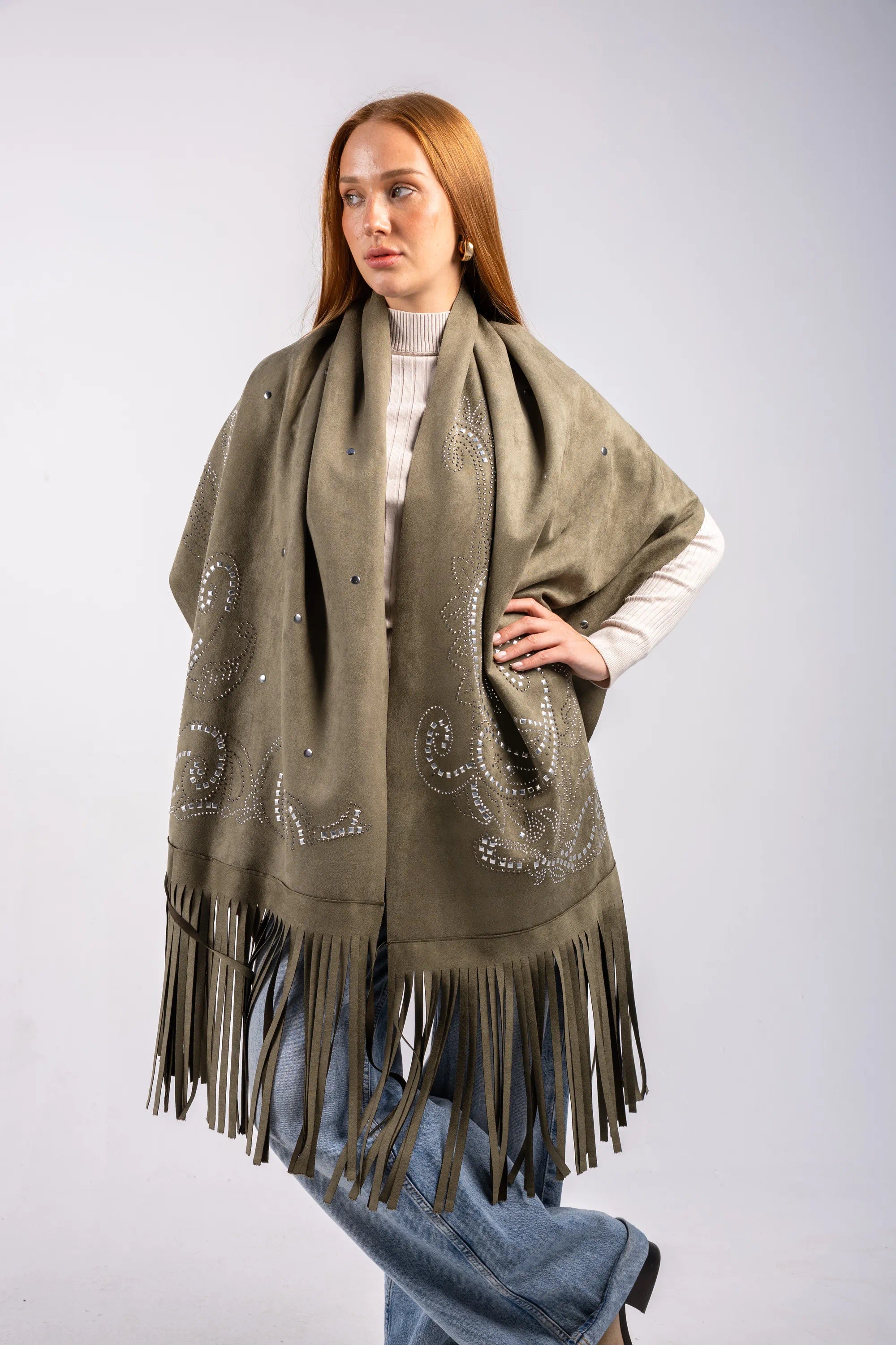 Woman wearing a green poncho with fringe details on a plain background