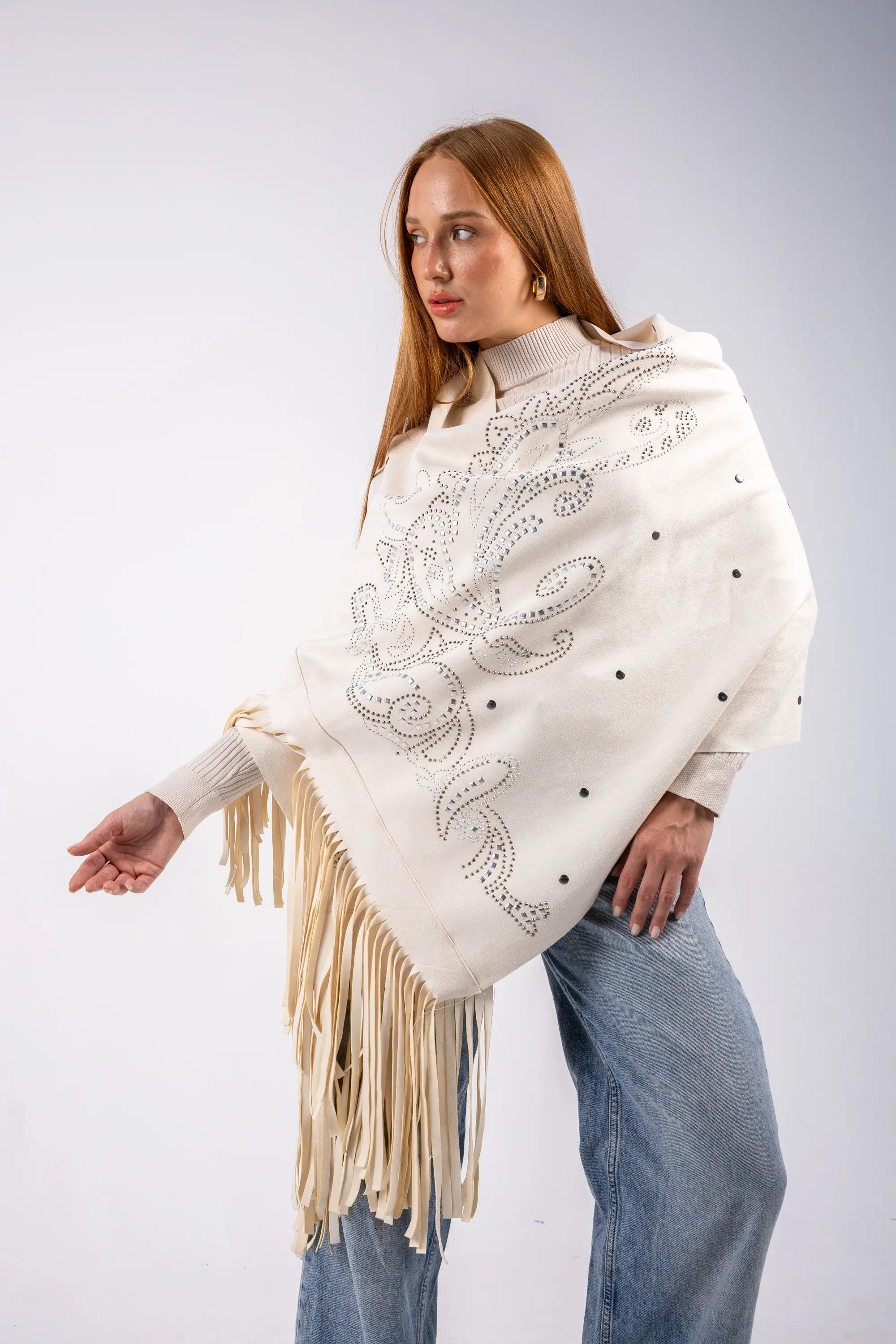 Woman wearing a white poncho with fringe and embroidery on a light gray background