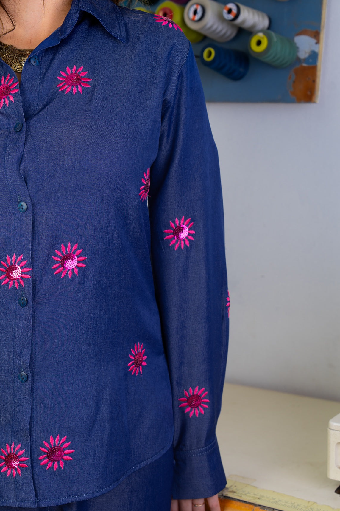 Blue shirt with pink floral patterns worn by a person, with sewing materials in the background.