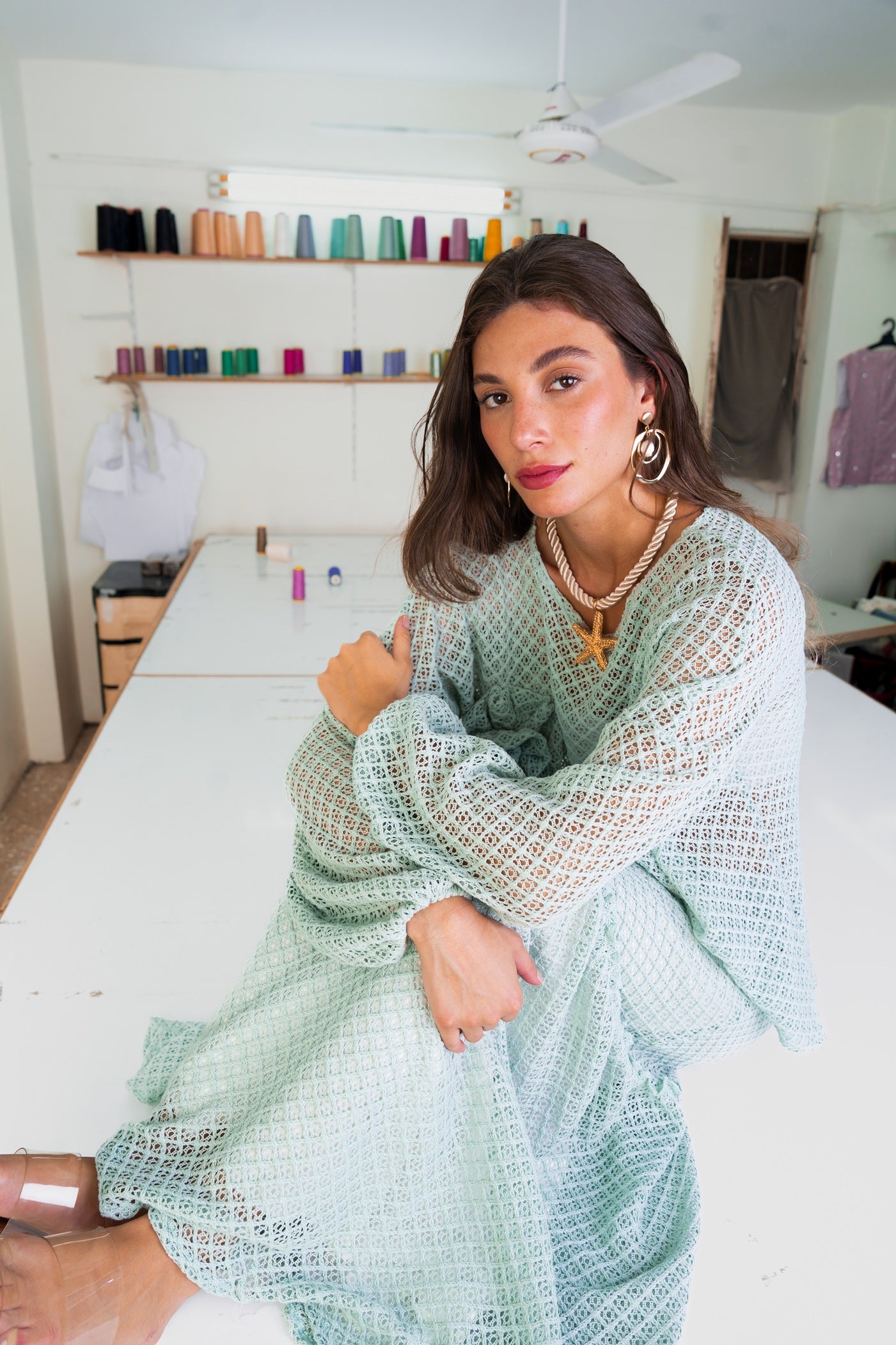 Woman in a light green dress sitting in a room with shelves in the background