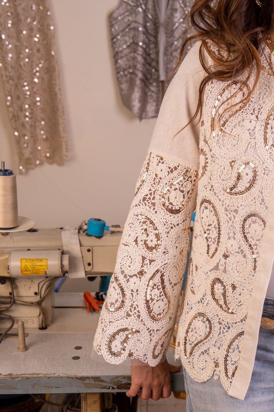 Person wearing a beige lace dress with sequin embellishments in a sewing workshop.