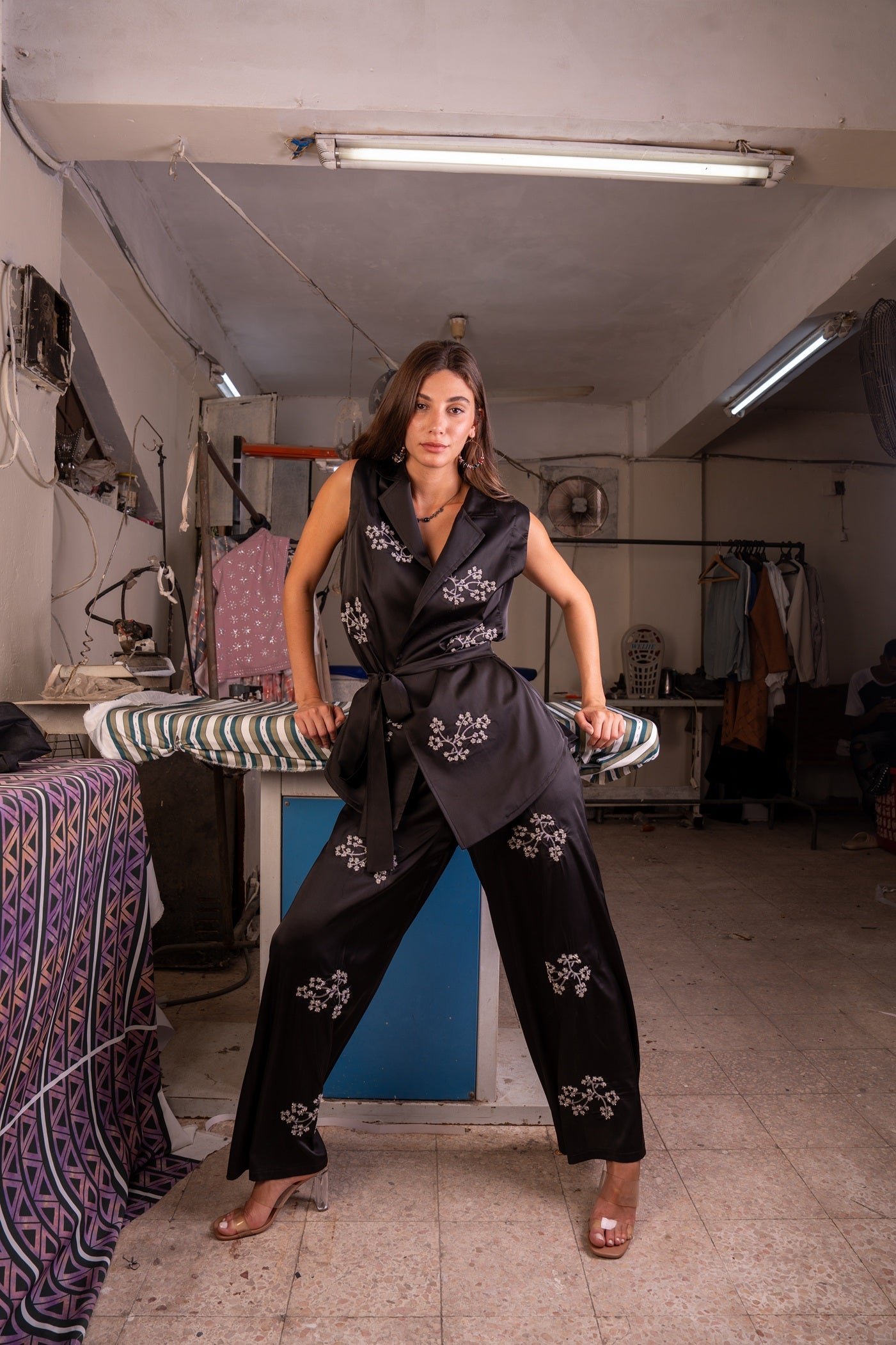 Woman in a black outfit with floral patterns standing in a workshop.