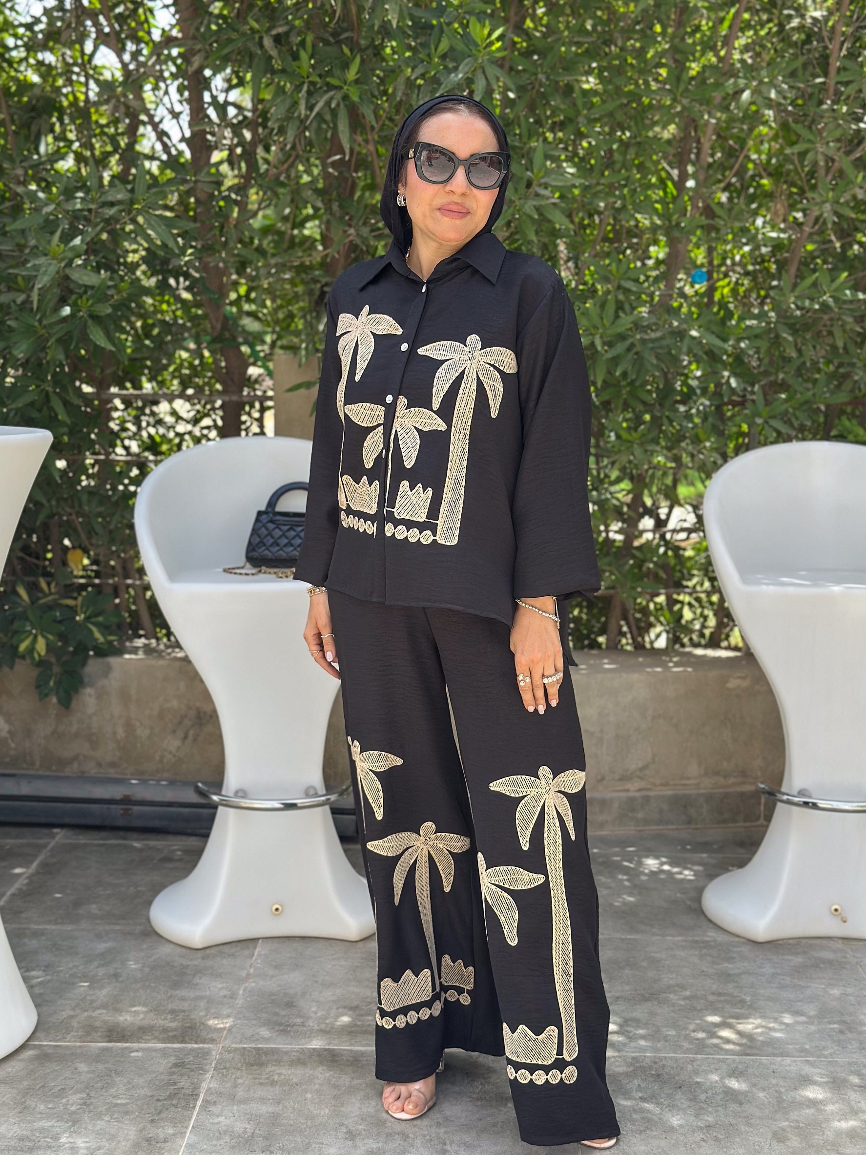 Woman wearing a black outfit with palm tree patterns outdoors.