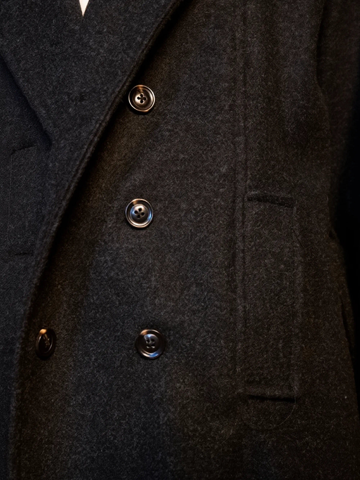 Close-up of a dark coat with brass buttons on a black background