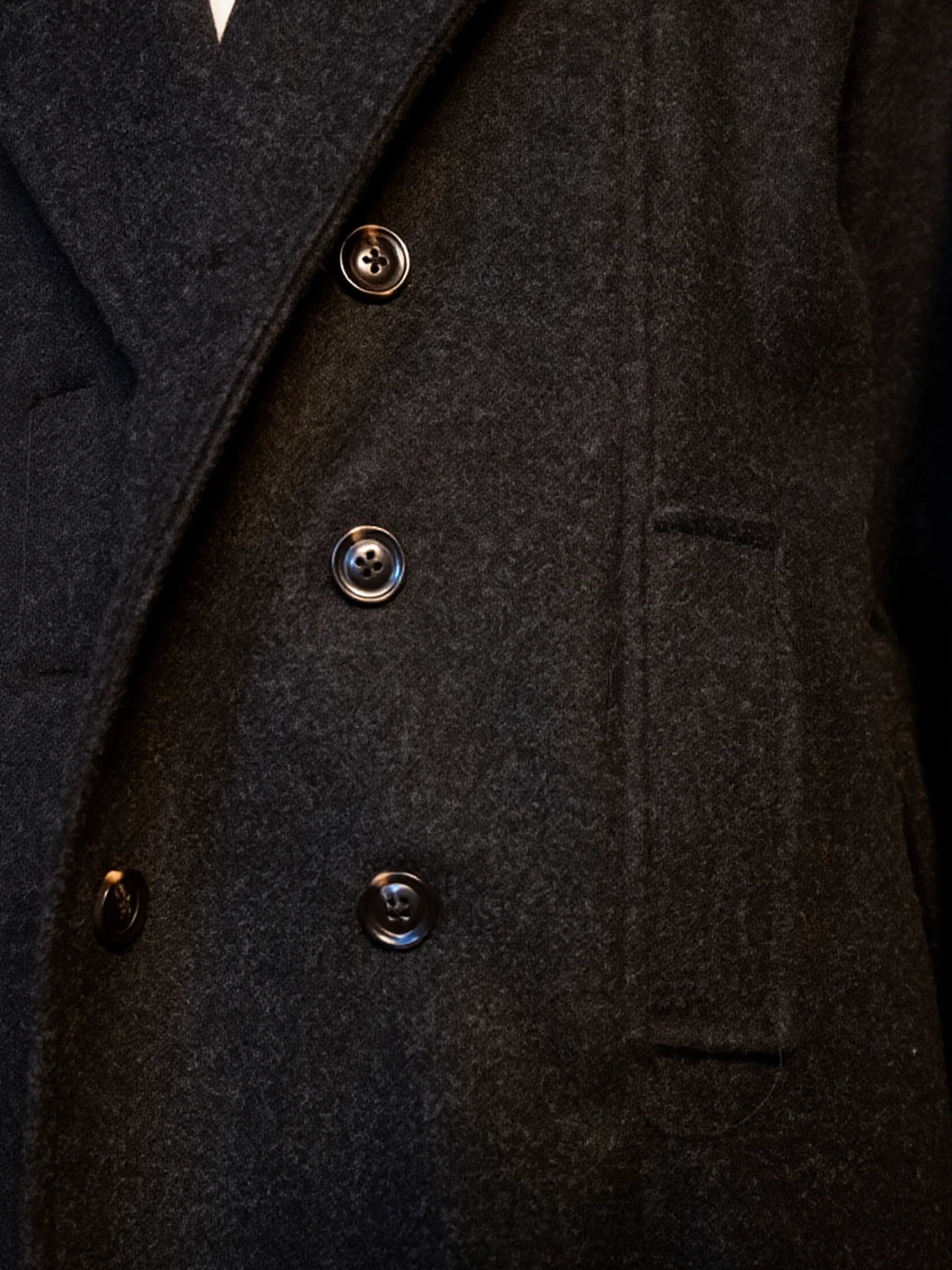 Close-up of a dark coat with brass buttons on a black background