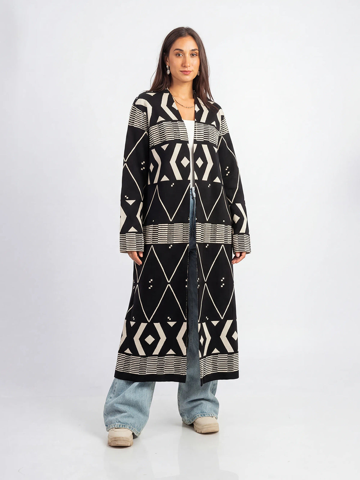 Woman wearing a long black and white patterned coat on a white background