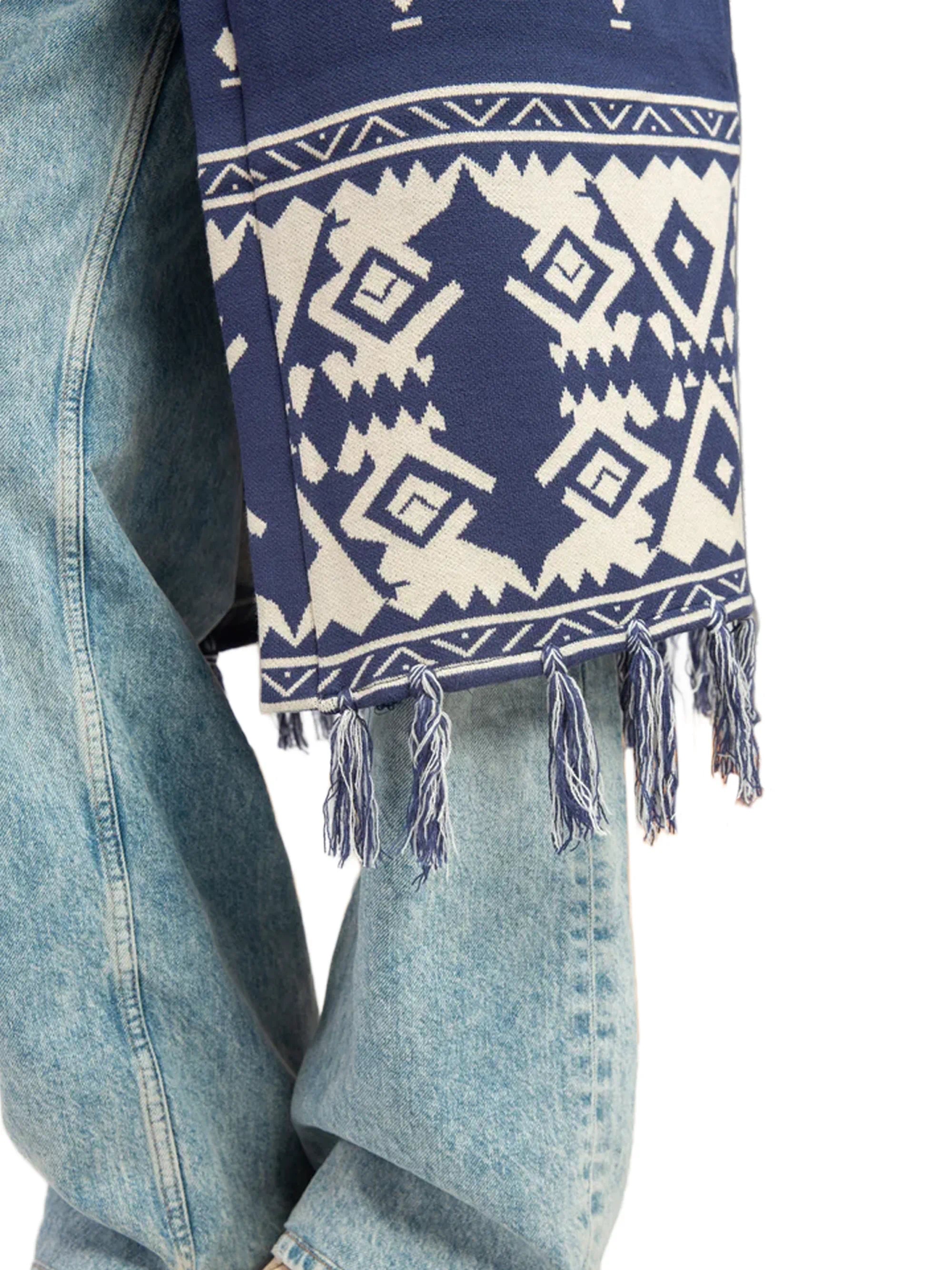 Navy blue and white patterned scarf with tassels draped over a denim jacket.