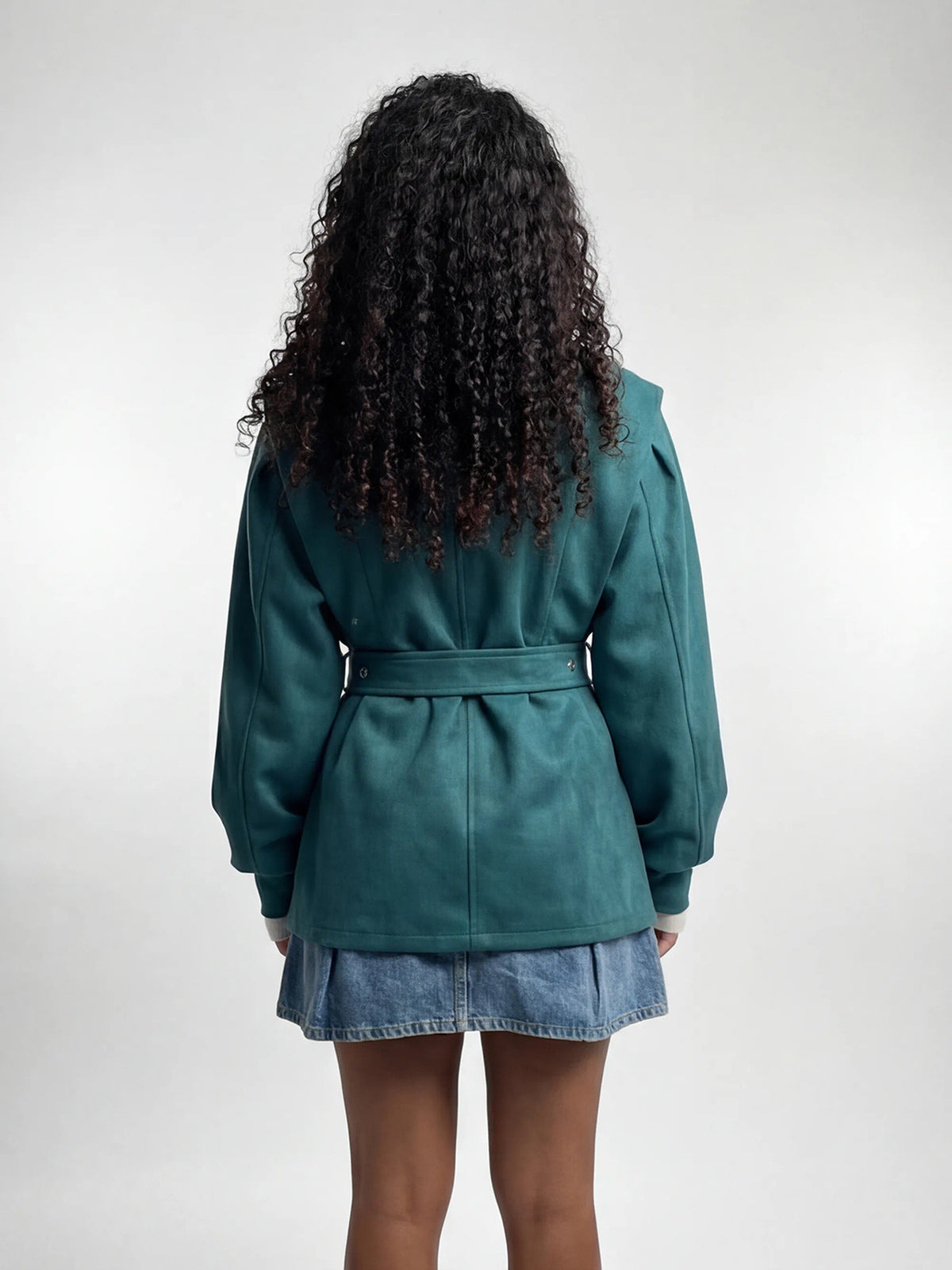 Person wearing a teal coat and denim skirt on a white background