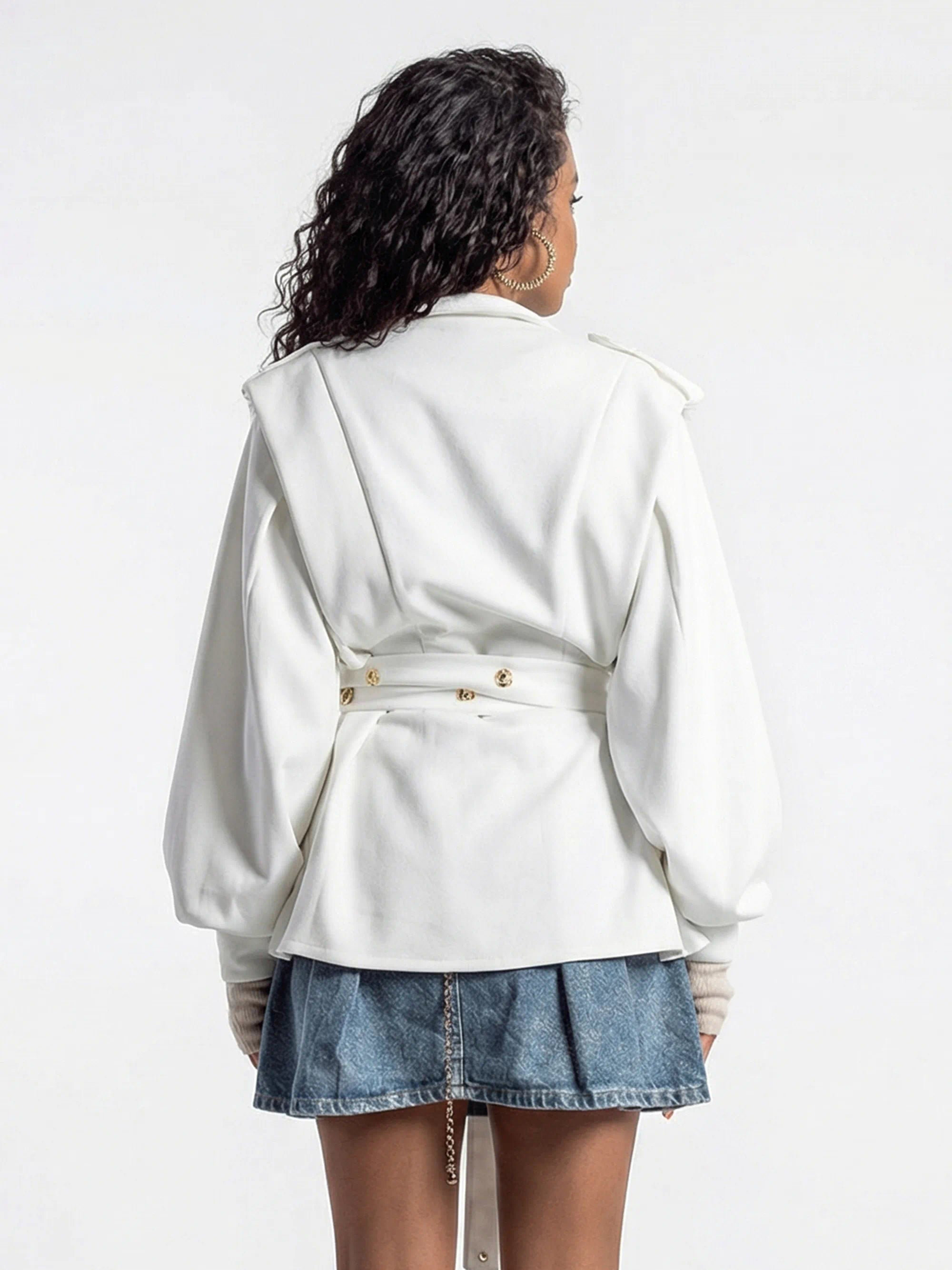 Person wearing a white trench coat over a denim skirt on a plain background