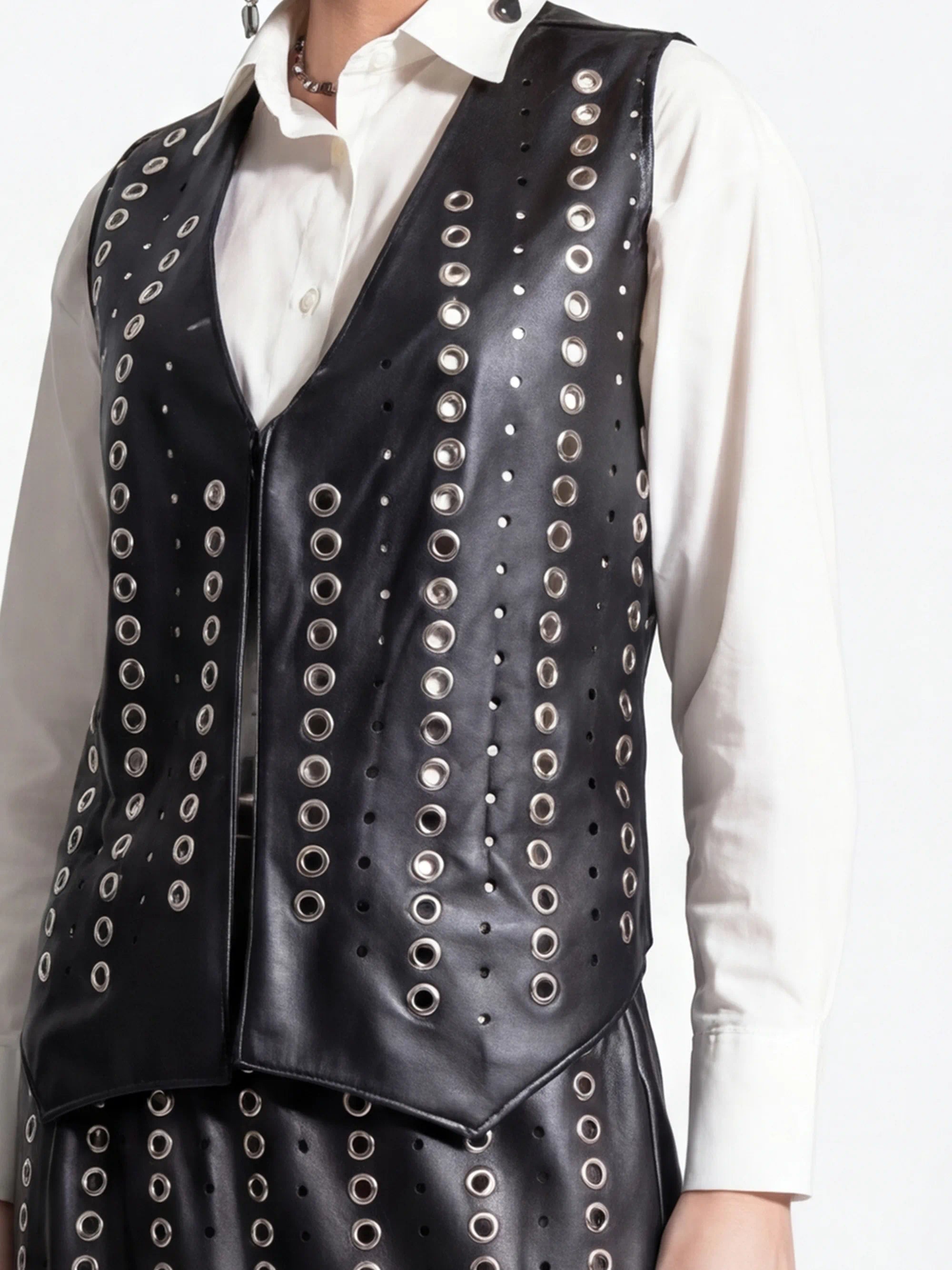 Black leather vest with silver studs worn over a white shirt on a white background