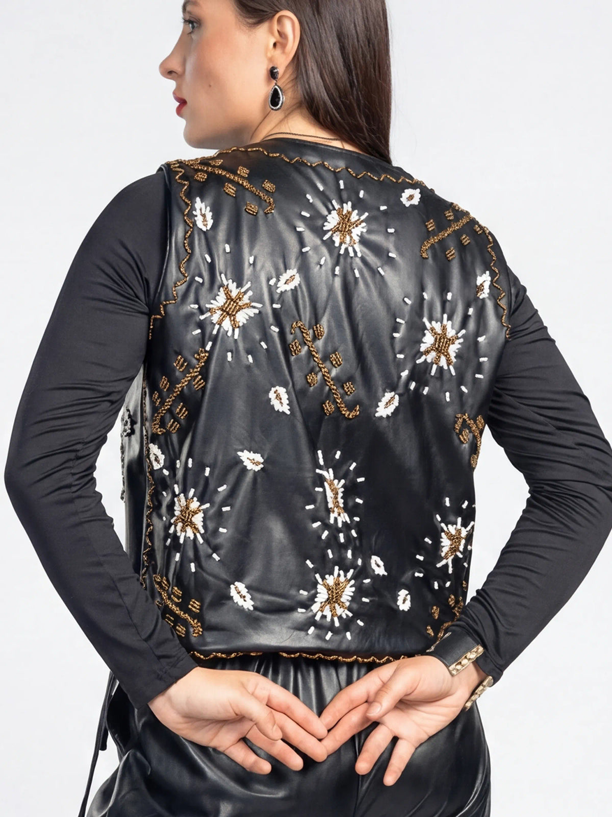 Woman wearing a black embroidered vest over a black long-sleeve shirt on a white background
