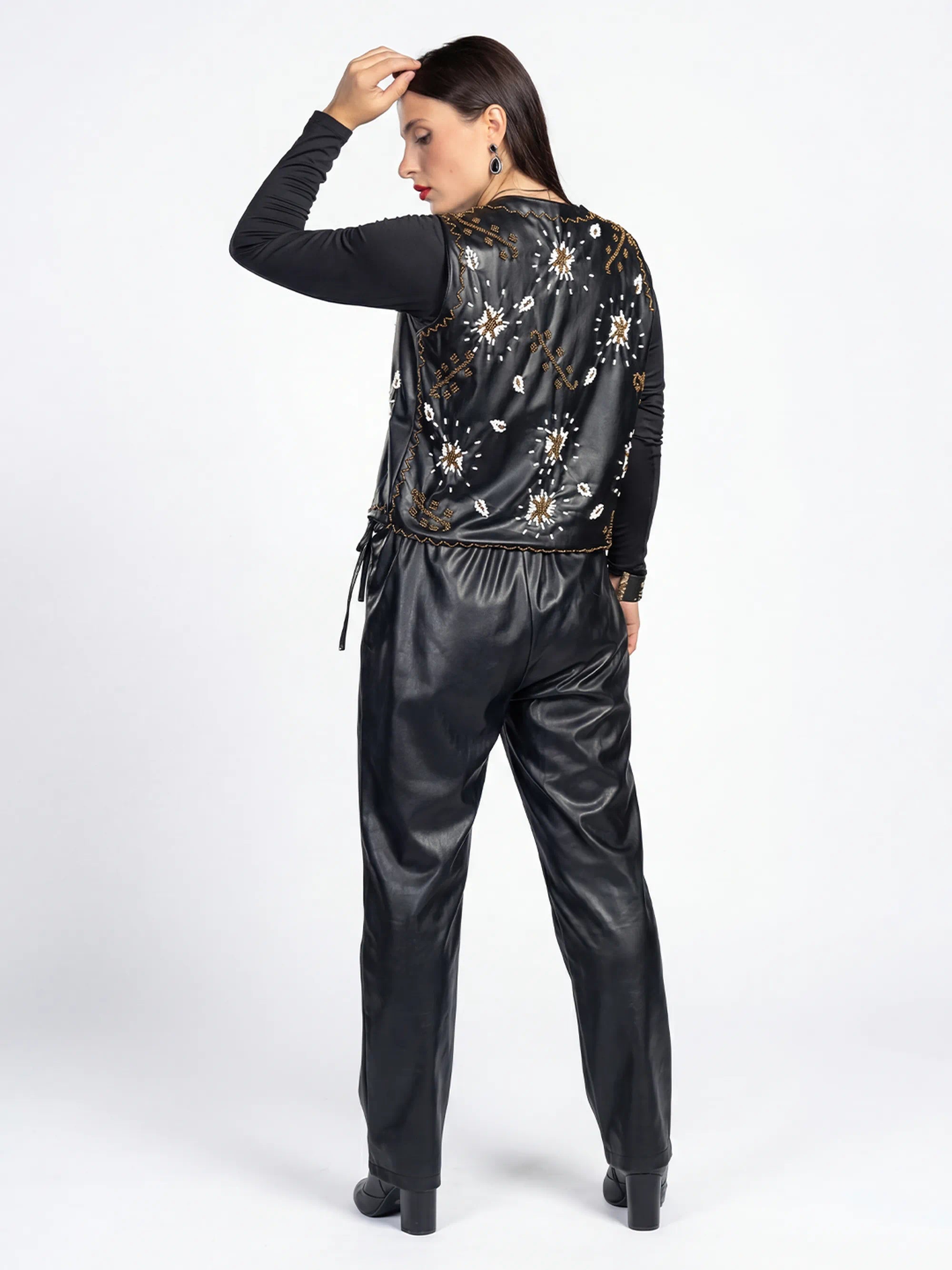 Woman wearing a black embroidered jacket and shiny black pants on a white background