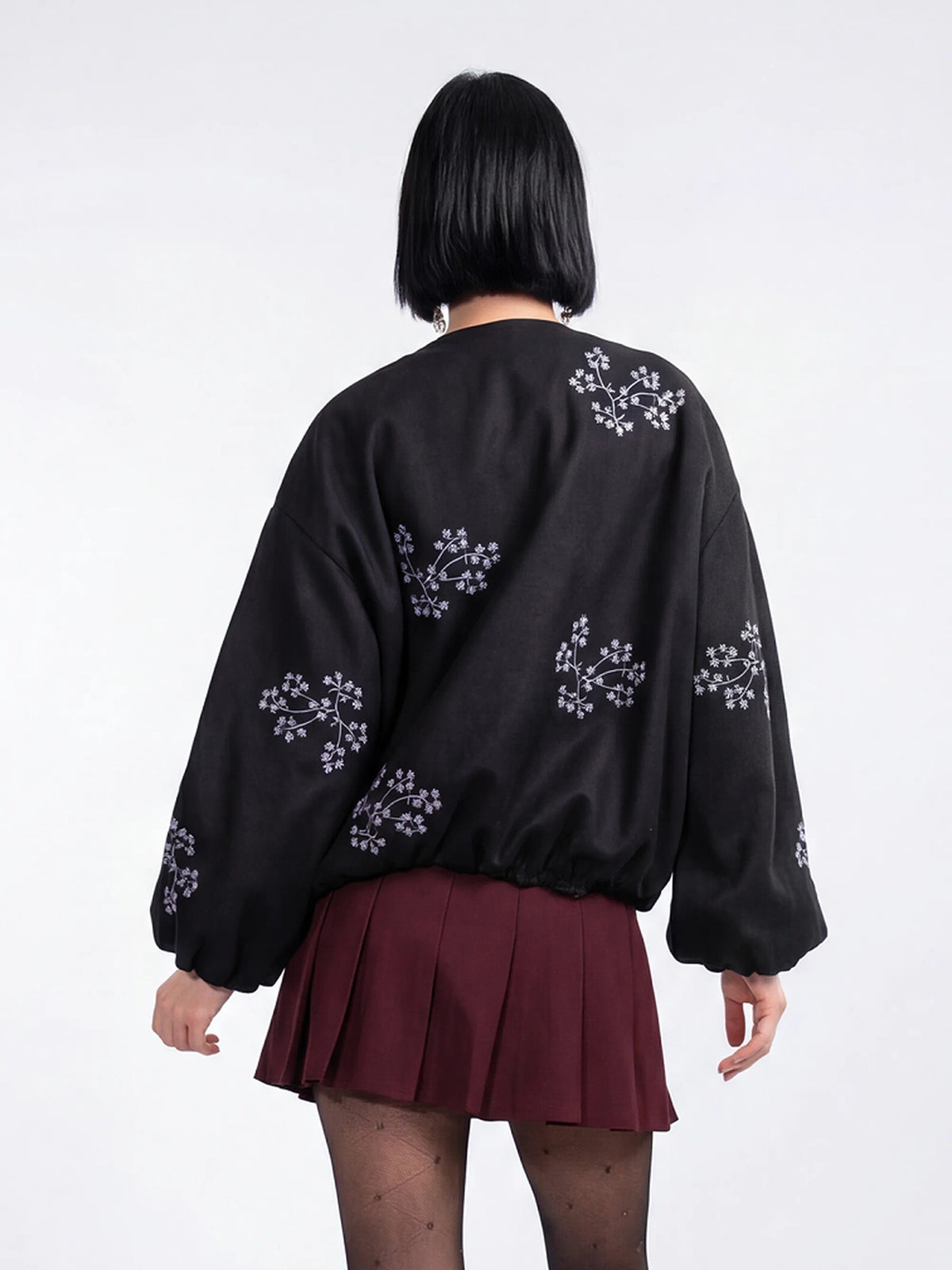 Person wearing a black embroidered top and maroon pleated skirt on a white background