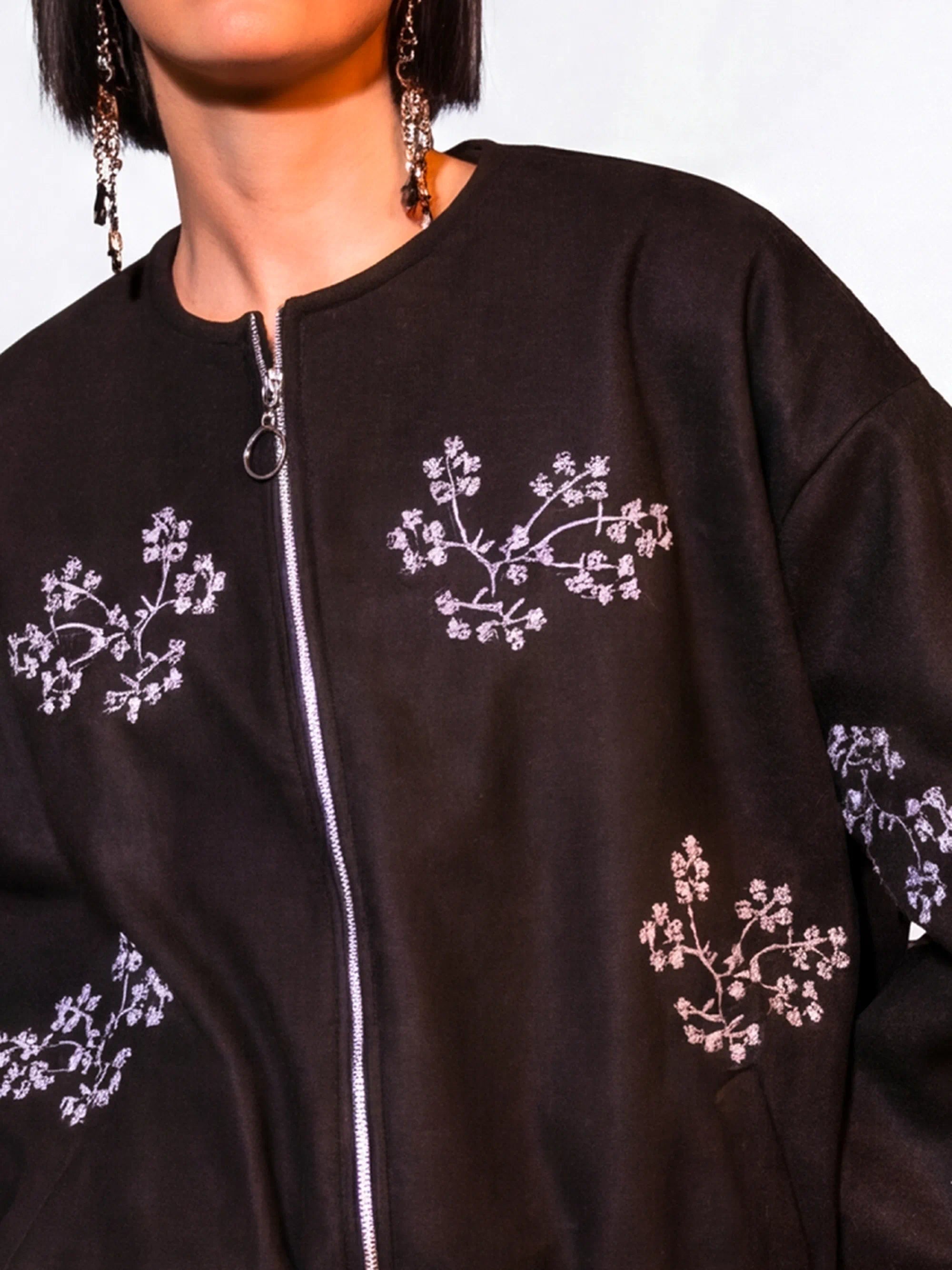 Black jacket with white floral embroidery on a plain background