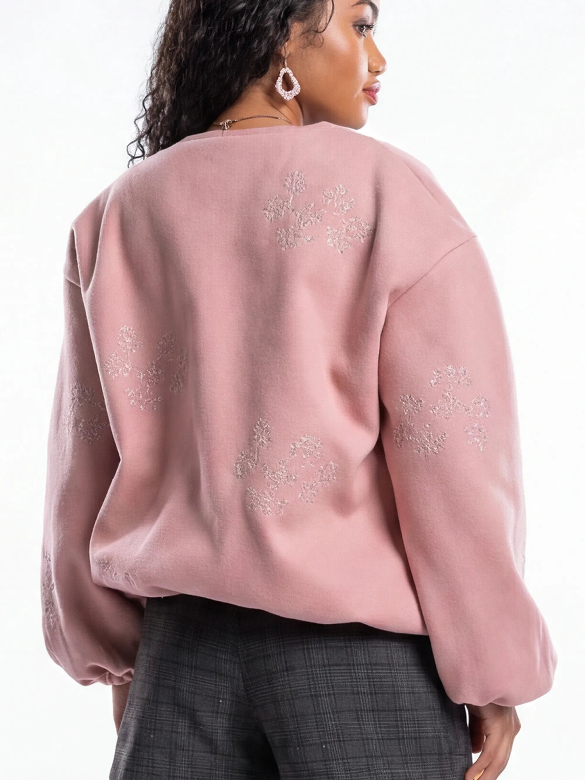 Pink sweater with floral embroidery worn by a person on a white background