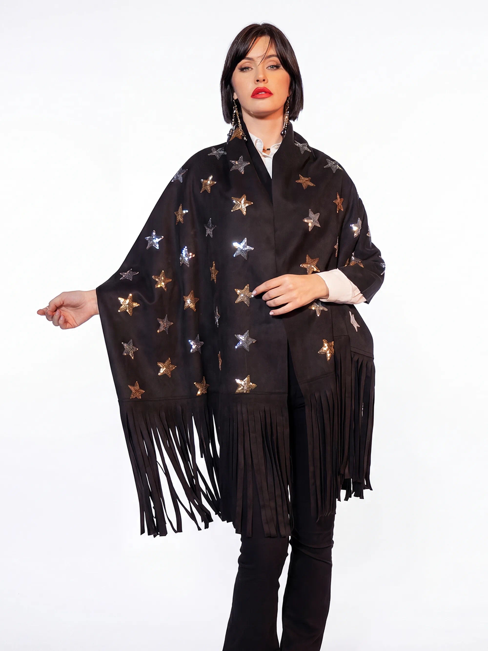 Woman wearing a black poncho with star patterns and fringes on a white background