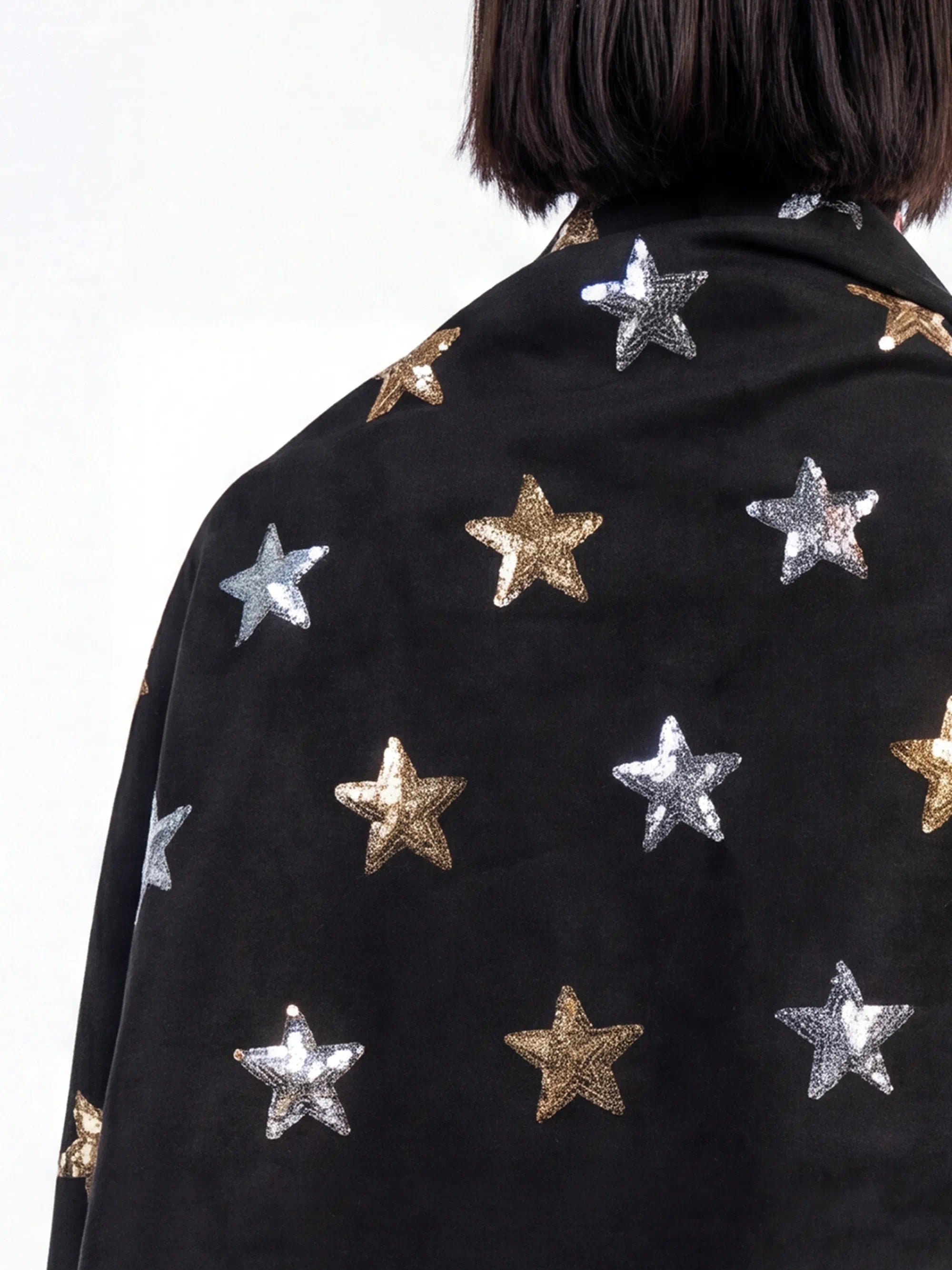 Black scarf with gold and silver star patterns worn by a person on a white background