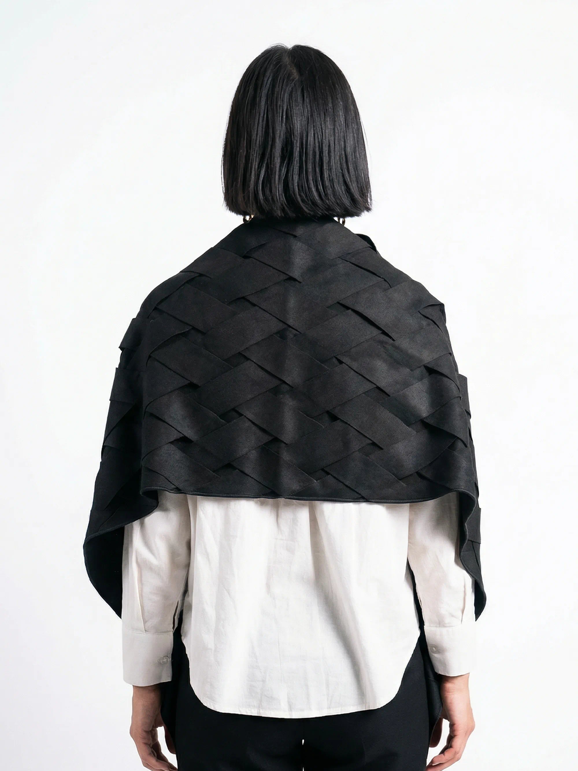 Person wearing a black woven shawl over a white shirt on a white background